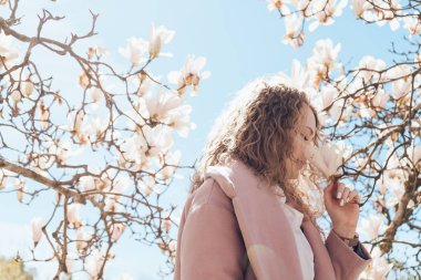 kıvırcık genç kadın parkta güzel kokulu bir çiçek açan Manolya koklama pembe bir ceket