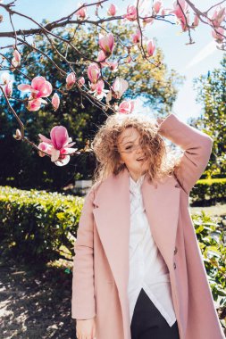 pembe bir ceket kıvırcık genç kadın gülüyor, sıcak bahar hava ve güneş Park sahiptir