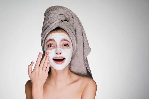 Gadis muda yang cantik dengan handuk di kepalanya, setelah mandi, menerapkan masker wajah melembabkan berguna — Stok Foto