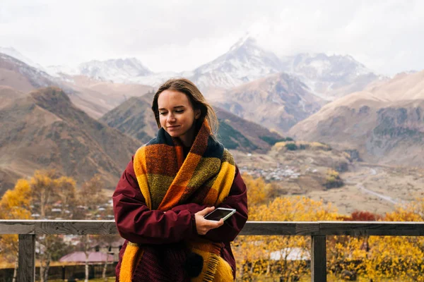 Ein nettes junges Mädchen ist unterwegs, in einem warmen Schal, auf einem Hintergrund majestätischer Berge stehend — Stockfoto