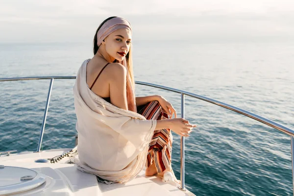 Elegáns fiatal lány a divatos nyári ruha ül ő fehér jacht jelentő és néz a kamerába — Stock Fotó