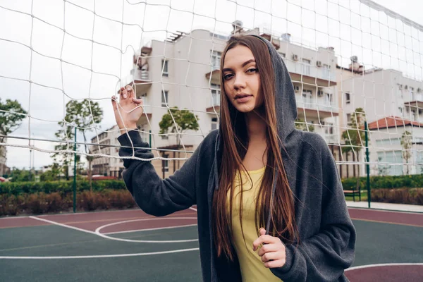 Fiduciosa ragazza snella che si esercita su un terreno sportivo all'aperto, in piedi vicino a una rete da pallavolo — Foto Stock