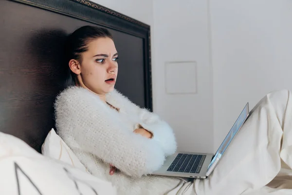Jong meisje zittend op bed laat in de nacht, horrorfilm kijken op haar laptop, ziet er bang — Stockfoto