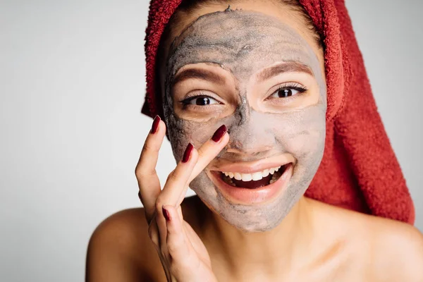 Gadis cantik tersenyum dengan handuk di kepalanya menerapkan masker tanah liat yang berguna di wajahnya — Stok Foto