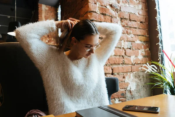 Joven freelancer seria chica en una chaqueta blanca y gafas está sentado en un café, trabajando — Foto de Stock