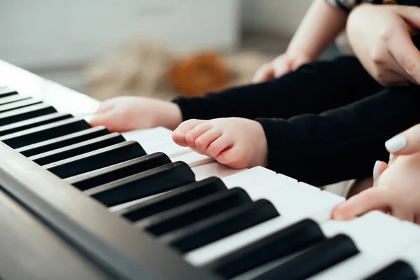 Заботливая молодая мать держит маленького ребенка на руках, учит ее играть на пианино — стоковое фото