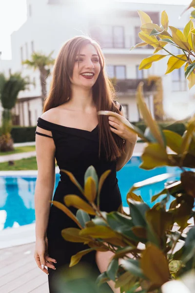 Ein luxuriöses langhaariges, reiches Mädchen im schwarzen Kleid schlendert durch ihren Garten, lächelt und genießt es, sich zu entspannen — Stockfoto