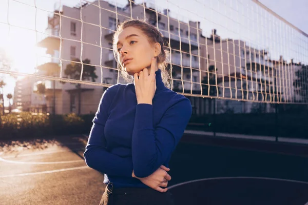 Vertrouwen stijlvolle meisje model in een blauwe trui poseren op een sportveld in de stralen van de ochtendzon — Stockfoto