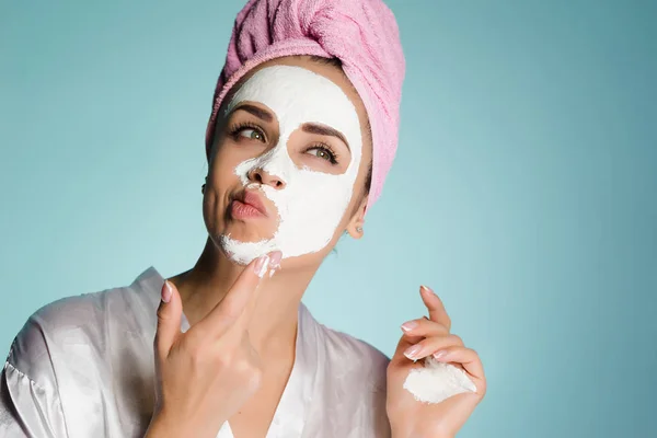 Carina ragazza con un asciugamano rosa sulla testa applicando una maschera idratante bianca sul suo viso — Foto Stock