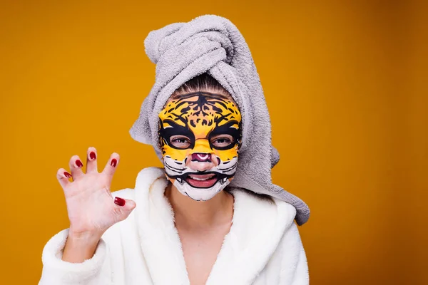 Uma jovem com uma toalha na cabeça e um roupão de banho branco ruge como uma besta, uma máscara com um rosto de leopardo no rosto — Fotografia de Stock