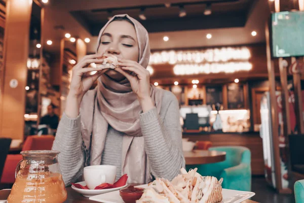 Éhes fiatal Arab lány hidzsáb ül a hangulatos kávézó ízletes ételt — Stock Fotó