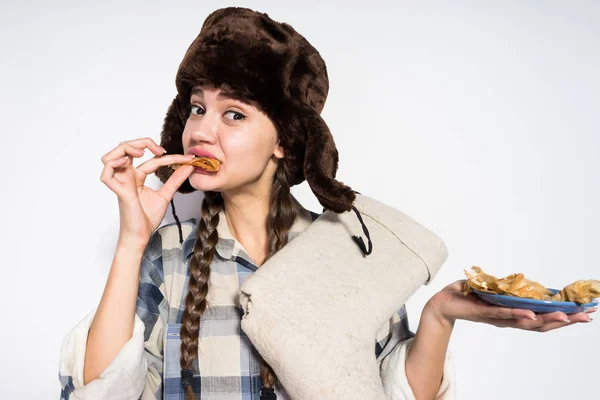 сочные русские телочки Голодная русская девушка в меховой шапке с нетерпением ест горячие блины, празднует карнавал, держит в руках зимние сапоги — Стоковое фото © mne_len #191991452