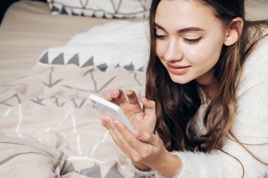 sevimli uzun saçlı kız yatakta yatıyor, rahatlatır ve rahatlatır, onun smartphone görünüyor