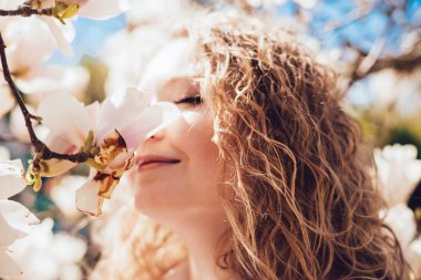 kıvırcık genç kız parkta, gülümser güzel kokulu bir çiçek açan Manolya burnunu çekmek, sıcaklık sahiptir