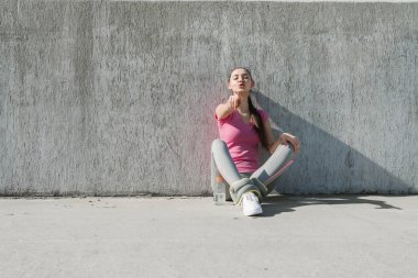 bir parmak kamera için gösterilen açık havada, yerde oturan sportif genç kız