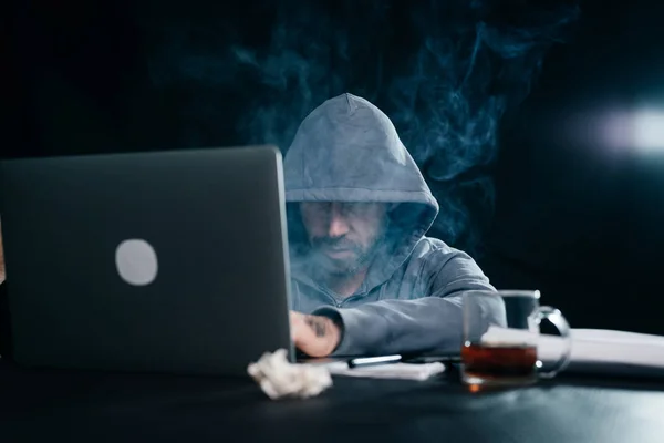 Misterioso criminoso homem com um capuz na cabeça hackear um laptop no escuro — Fotografia de Stock