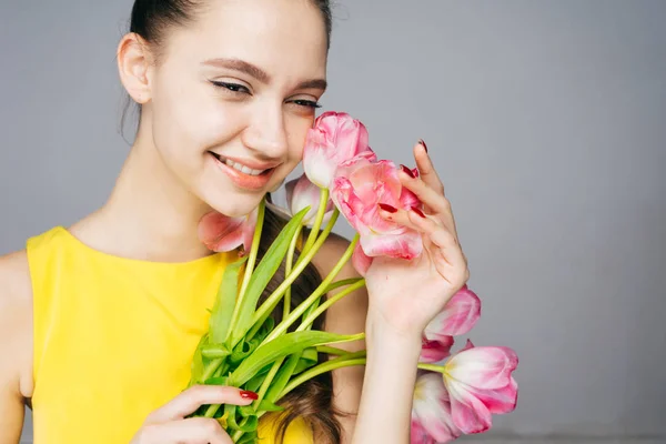 Mutlu sarı elbiseli genç kız gülümser ve güzel kokulu pembe çiçekler buket tutar — Stok fotoğraf