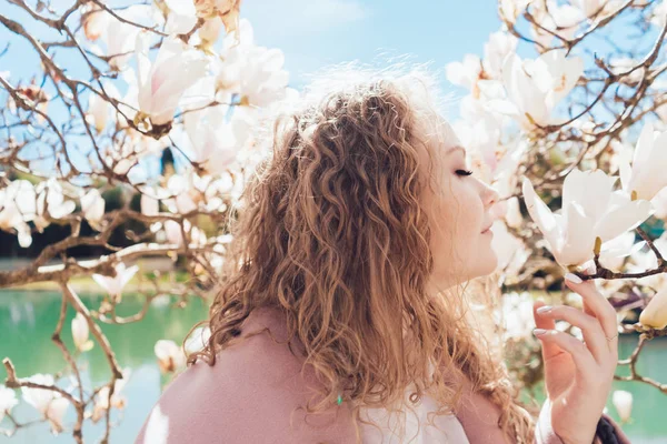 Chica rizada atractiva huele una magnolia floreciente aromática en un parque en los rayos del sol — Foto de Stock