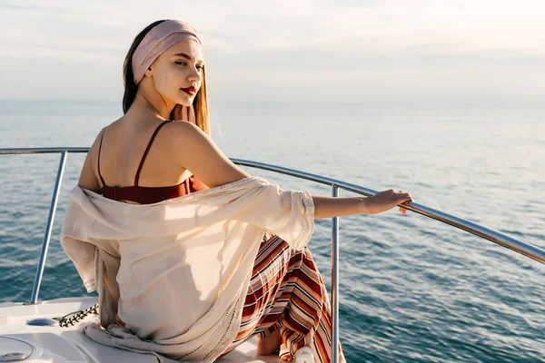 Hermosa joven con un pañuelo en la cabeza sentado en un yate blanco, posando y mirando a la cámara en el sol —  Fotos de Stock