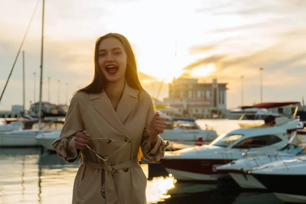 Szczęśliwy atrakcyjna dziewczyna w modny płaszcz stoi na port morski i śmiech — Zdjęcie stockowe