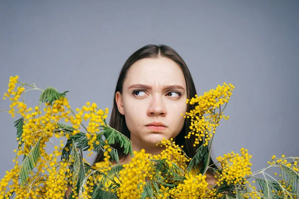 Jovem insatisfeito segurando um grande buquê de mimosa amarela, uma alergia às flores — Fotografia de Stock