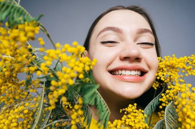 güzel kokulu sarı Mimoza tutan gülümseyerek, beyaz dişler, mutlu genç kız