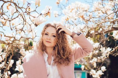 Bahar ve güneş güzel kokulu magnolia, bir arka plan üzerinde bir parkta poz kıvırcık genç kadının