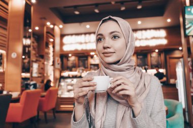 bir kafede otururken, hoş kokulu kahve içme ve hakkında bir şey düşünüyor bir başörtüsü güzel Arap kızla