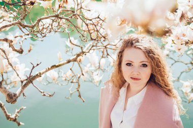 kıvırcık zarif kız pembe ceket bahar bahçe, çiçek açan Manolya ve gölet yanında poz