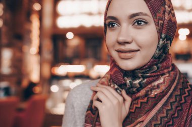 rahat bir oryantal kafede oturan ve gülümseyen bir başörtüsü güzel Arap kızla