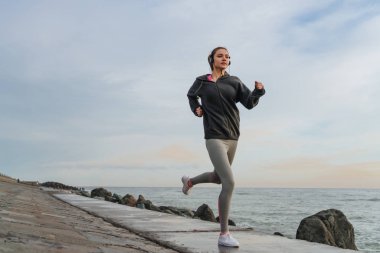 Etkin atletik kız çalışır etrafında kulaklıklar, denizde güzel bir ince rakam istiyor