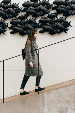 Merdivenlerden alışılmadık bir duvar arka planı gri moda ceket şık kentsel kız yükseltir