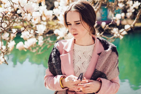 Belle fille élégante se tient dans un parc au soleil, entouré d'arbres verts, temps chaud de printemps — Photo