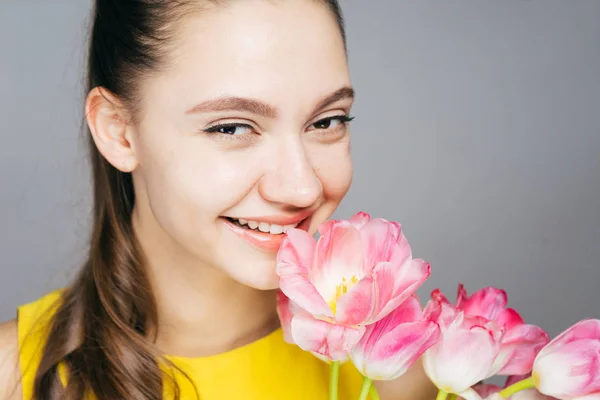 Mooi jong meisje in gele jurk lacht, houden van geurige roze bloemen — Stockfoto