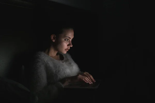Giovane ragazza si siede a letto al buio di notte e guarda film interessante sul suo computer portatile — Foto Stock