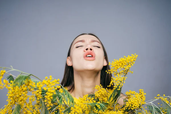 Молодая девушка держит желтую мимозу и чихает, аллергия на цветы — стоковое фото