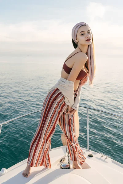 Hermosa mujer rica en ropa de verano elegante posando en su yate blanco contra el mar azul calma —  Fotos de Stock