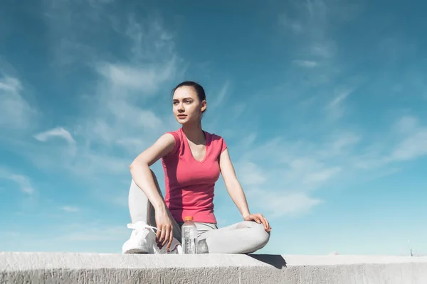 Sebevědomý, cílevědomé děvče sedí pod modrou oblohou, odpočívá po tréninku, získává na síle — Stock fotografie