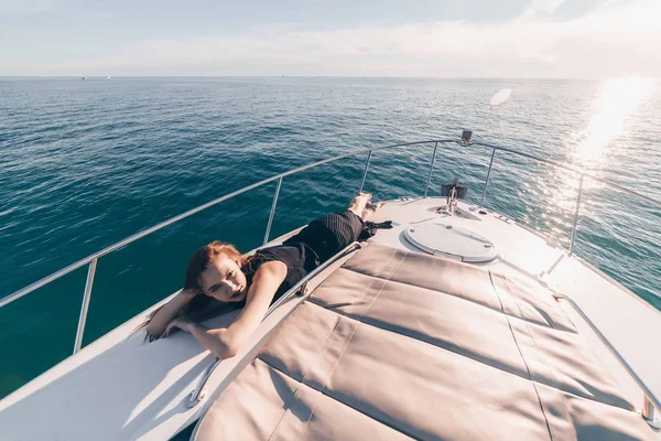 Роскошная богатая женщина в черном платье покоится на своей белой яхте на солнце, морское путешествие — стоковое фото
