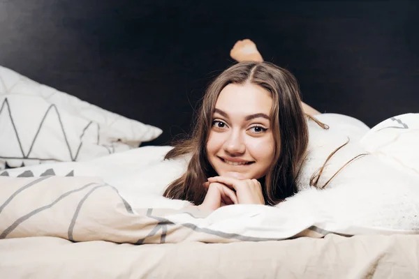 Αστεία νεαρή κοπέλα ξαπλωμένη στο κρεβάτι, ανάπαυσης, βλέπουν τα φωτογραφικών μηχανών και χαμογελαστός — Φωτογραφία Αρχείου