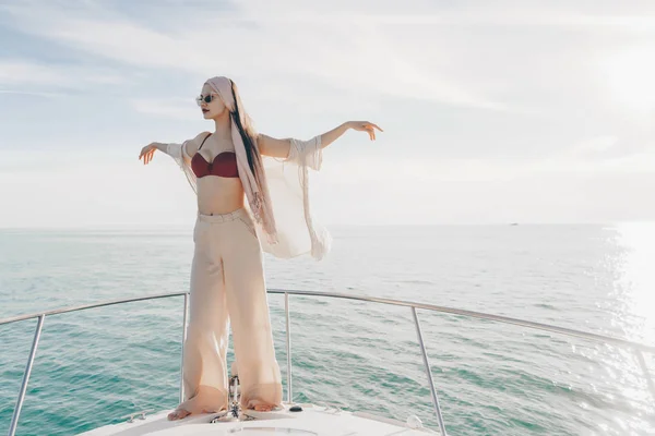 Stylische junge Frau in Sommerkleidung posiert auf ihrer weißen Jacht und bläst einen warmen Wind — Stockfoto