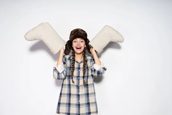 Laughing young Russian girl with pigtails in a fur hat holds gray felt boots — Stock Photo, Image