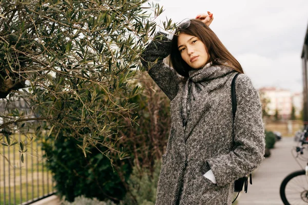 Jeune fille urbaine aux cheveux foncés en manteau gris tendance posant à l'extérieur, style de rue — Photo