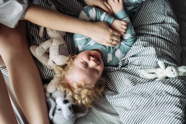 Mamá juega con su pequeño bebé, ríe, hace cosquillas, se acuesta en la cama — Foto de Stock