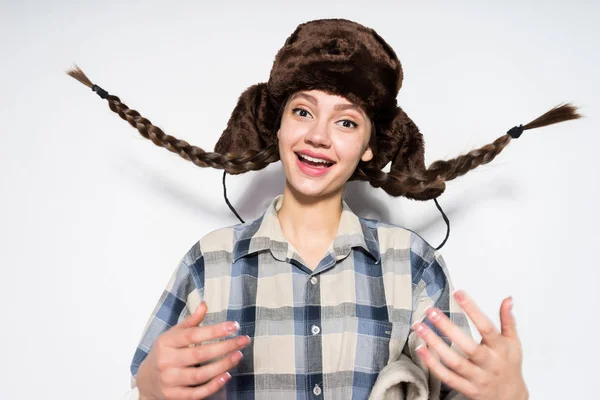 Alegre chica rusa con coletas, en un cálido sombrero de piel mira a la cámara y sonríe, espera el invierno — Foto de Stock