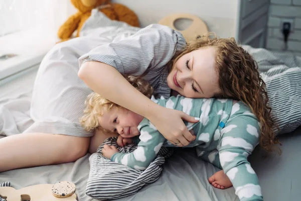 Glücklich freundliche Familie, junge Mutter spielt mit ihrem kleinen Sohn, auf dem Bett liegend — Stockfoto