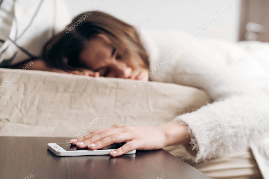 sleepy young girl sleeping in bed, can not hear the alarm on her smartphone