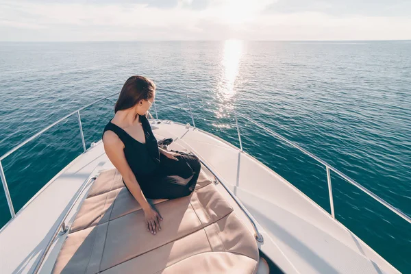 Богатая стильная девушка в черном платье сидит на своей белой яхте, плывет на остров по морю — стоковое фото
