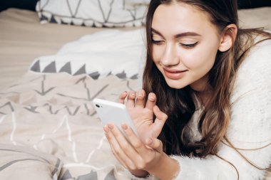 güzel genç kız yatakta dinlenme, onun smartphone bir mesaj yazma, yalan söylüyor
