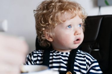 Kahvaltı küçük kıvırcık oğlu mavi gözlü bir yüksek sandalyede oturuyor